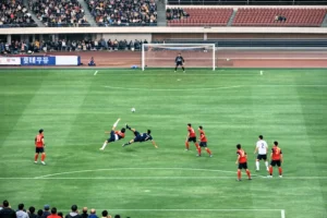 L'azione della doppia rovesciata ripresa da una prospettiva più ampia a centrocampo, che mostra il posizionamento delle due squadre e la traiettoria del pallone verso l'area di rigore.