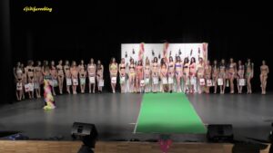 Un'ampia inquadratura panoramica che ritrae tutte le partecipanti di Miss Fragola 2016 schierate sul palco durante la serata finale. Le numerose concorrenti posano insieme indossando gli abiti della sfilata, creando un colpo d'occhio colorato e vivace che riempie l'intera scena. Al centro del gruppo si distingue la vincitrice Valentina Ceccato con la fascia ufficiale. L'immagine cattura l'atmosfera festosa dell'evento, con le luci di scena e le scenografie a tema che fanno da cornice a questo momento collettivo di bellezza e condivisione.
