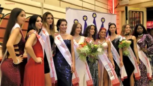 Fotografia delle dieci concorrenti premiate del concorso Principessa d’Europa durante la proclamazione ufficiale. Le partecipanti indossano abiti da sera e fasce con la dicitura Principessa d’Europa – Finalista Nazionale. Al centro è presente la vincitrice, riconoscibile dalla corona e dal bouquet di fiori, mentre le altre finaliste posano ai suoi lati con postura elegante. Sullo sfondo si vede il grande banner dell’evento, decorato con una corona stilizzata e stelle, insieme ai loghi degli sponsor. L’immagine documenta il momento celebrativo della premiazione delle finaliste nazionali.