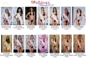 Fotografia di un gruppo di finaliste di Miss Venice Beach 2019 disposte in due file su un palco. Le concorrenti indossano bikini neri e fasce identificative con nome, età, città di provenienza e altezza. Sullo sfondo è visibile il pannello ufficiale del concorso con la scritta “Miss Venice Beach 2019”. Le partecipanti, illuminate dalle luci di scena, posano frontalmente per la foto di presentazione. L’immagine documenta una parte delle finaliste selezionate per la serata conclusiva.