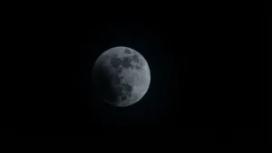Fotografia della Luna durante l’eclissi parziale del 28 agosto 2026, nella fase di copertura di circa il 25%. Il disco lunare appare per la maggior parte illuminato, con una porzione in ombra visibile sul lato sinistro. I dettagli dei mari lunari e dei crateri sono nitidi, mentre il cielo circostante è completamente nero. L’immagine documenta la fase iniziale dell’ingresso della Luna nell’ombra terrestre.